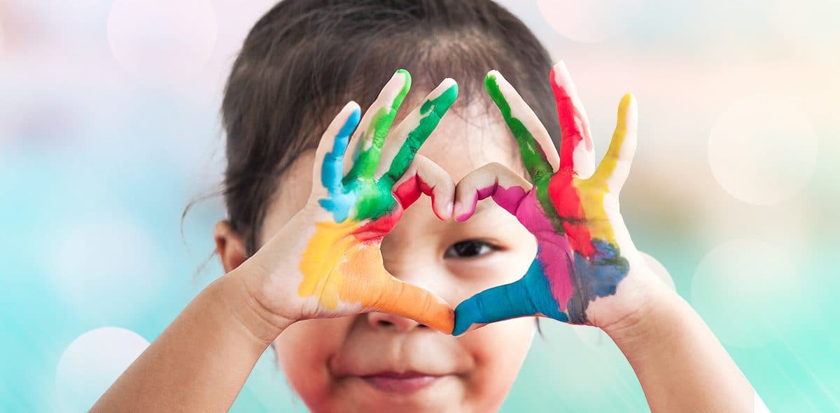 A child making a heart shape with paint-covered hands